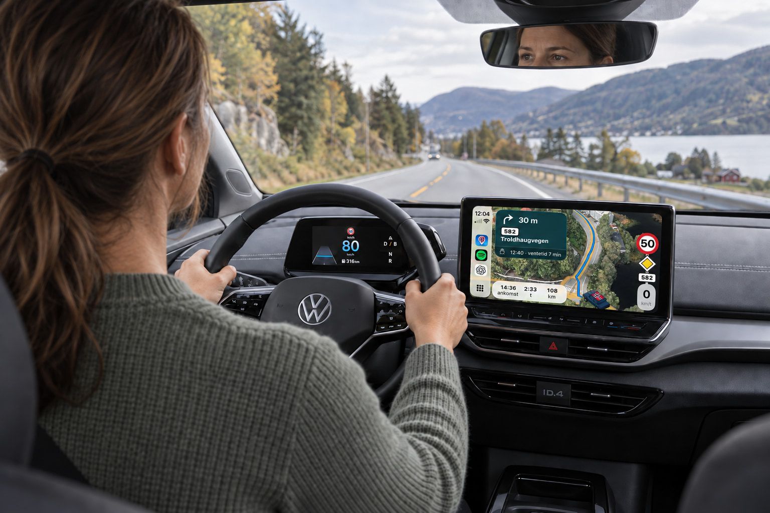 En sjåfør kjører langs fjorden i en Volkswagen ID.4 med Vegferd i CarPlay på bilskjermen: svingkort mot Troldhaugvegen, ferjefeltet og skiltstolpen med fartsgrense 50